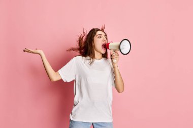 Portrait of young girl in white t-shirt shouting in megaphone against pink studio background. Important news. Information. Concept of youth, emotions, facial expression, lifestyle clipart