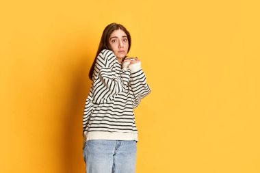 Çizgili kazaklı genç kızın stüdyo portresi. Gözlerinde küçük bir korkuyla poz veriyor. Sarı sırtlı. Utangaç ve kararsız hissediyorum. Gençlik kavramı, duygular, yüz ifadesi, yaşam tarzı