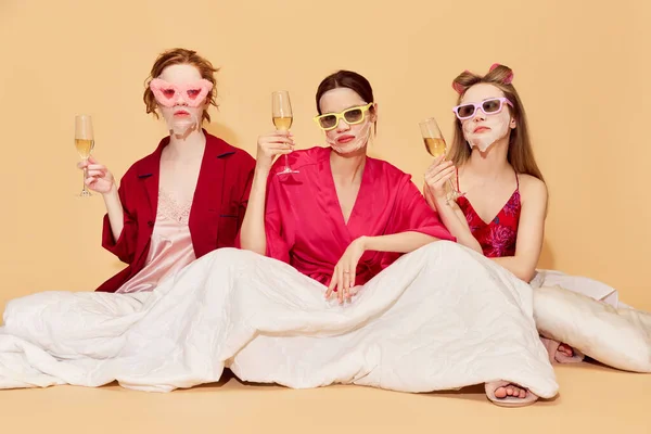 穿着睡衣 戴着面具 穿着时髦而又漂亮的少女们 坐在毛毯下过夜 喝着香槟 感情的概念 — 图库照片