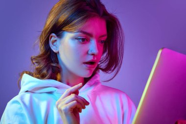 İlgi ve heyecanla tablete bakan güzel bir genç kızın yakın plan görüntüsü, neon ışıkta mor arkaplanda haber okuyor. Duygular, gençlik, yaşam tarzı, eğitim, serbest meslek kavramı