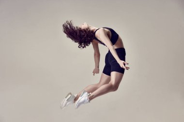 Spor giyinen, atlayan, gri stüdyo geçmişine karşı hareket eden genç ve güzel bir kadının dinamik görüntüsü. Spor yaşam tarzı, güzellik, vücut bakımı, fitness, sağlık
