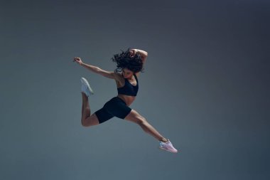 Hareket halinde. Hareket sanatı. Gri stüdyo geçmişine karşı zayıf, formda vücut eğitimi almış çekici genç bir kadın. Atlıyorum. Spor yaşam tarzı, güzellik, vücut bakımı, fitness, sağlık