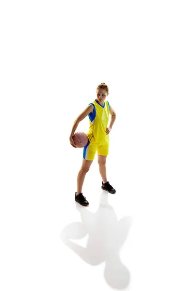 白いスタジオを背景にボールを背景にした黄色の制服姿の女子バスケットボール選手の全長像 アイソメトリックビュー プロスポーツ 健康的なライフスタイル 趣味の概念 — ストック写真