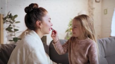 Hazırlanıyorum ve eğleniyorum. Mutlu anne ve küçük kız evde, çocuk kadına ruj sürüyor. Mutluluk. Aile ilişkisi kavramı, annelik ve çocukluk, sevgi, şefkat.