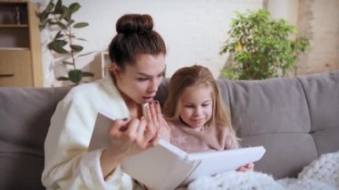 Küçük tatlı kızı ve kızıyla kanepede oturan ve kitap okuyan, gündüzleri evde peri masalları okuyan genç bir kadın. Gülümseme, mutluluk. Aile ilişkisi, annelik, çocukluk, aşk, şefkat kavramı