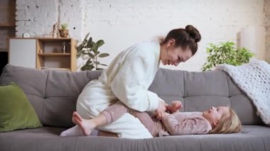 Eğleniyorum. Genç bir kadın, mutlu bir anne, küçük bir kızla oynuyor, kızı evde kanepede yatıyor. Sarılın, sevginizi gösterin. Aile ilişkisi kavramı, annelik ve çocukluk, sevgi, şefkat.