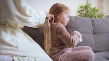 Sevecen anne, gündüzleri küçük kızıyla evde vakit geçiriyor. Kanepede oturup örgü örmek. Aile ilişkisi kavramı, annelik ve çocukluk, sevgi, şefkat.