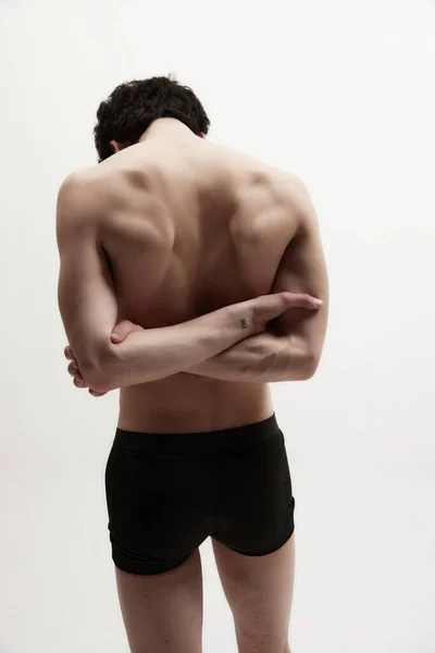 Relief, strong, muscular back. Rear view of young man posing shirtless, in black underwear against white studio background. Healthy spine. Concept of male body aesthetics, style, fashion, mens beauty