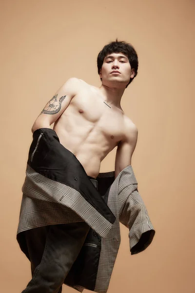 Portrait of young handsome asian man posing shirtless with stylish grey jacket against studio background. Style. Concept of male body aesthetics, style, health, mens beauty and fashion