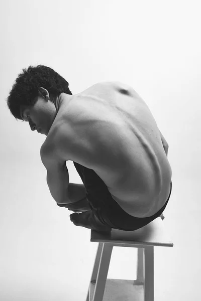 后视镜图像 年轻男子穿着黑色裤子 赤身裸体地坐在高椅子上 背对着白色的工作室背景 男性身体美学 男性美的概念 — 图库照片