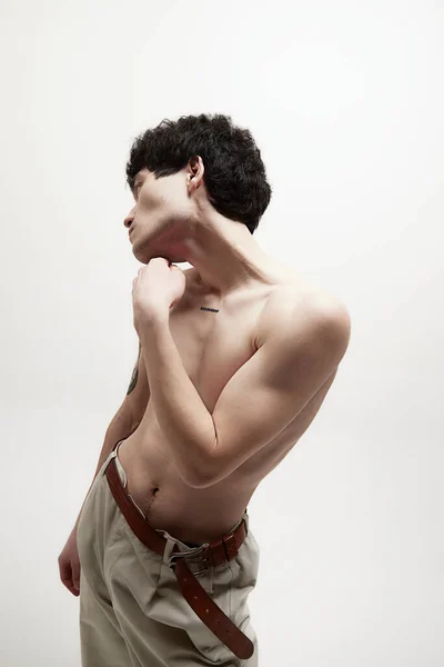 白いスタジオの背景にベージュのパンツに身を包んだ若いハンサムな男の肖像画 男性の体の美学 スタイル ファッション メンズ美しさの概念 — ストック写真