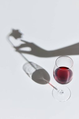 Romantik bir randevu. Kırmızı şarap kadehi beyaz arka planda, kadın eli ve gülü gölgesinde duruyor. Zevk anlayışı, alkol, şarap molası, çeşitlilik, şarap yapımı. Düz yatıyordu