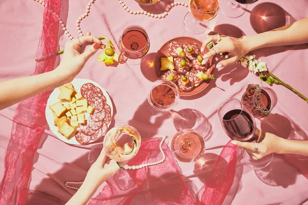 Hen party. Female hands with glassed with red and rose wine on pink textured background, tablecloth with appetizers, snacks. Taste, alcohol, wine degustation, celebration, winemaking concept. Flat lay