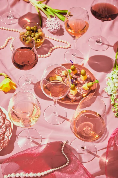 Glasses with red and pink delicious wine standing on tablet with appetizers, olives on pink textured background, tablecloth. Taste, alcohol, wine degustation, celebration, winemaking concept. Flat lay