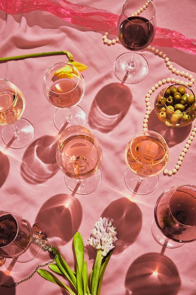 Glasses with red and pink delicious wine standing on tablet with appetizers, olives on pink textured background, tablecloth. Taste, alcohol, wine degustation, celebration, winemaking concept. Flat lay