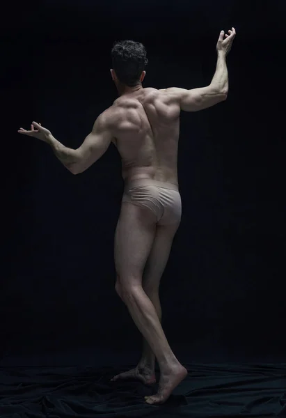 Full-length rear view portrait of handsome muscular shirtless man with relief strong body posing against black studio background. Concept of male body aesthetics, mens beauty, inspiration, art