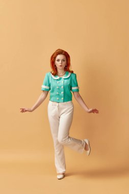 Turuncu stüdyo arka planına poz veren güzel, kızıl saçlı, şık elbiseli genç bir kadının tam boy portresi. Eski tarz, moda, güzellik, zarafet, 60 'lar, gençlik kavramı. Pin-up tarzı