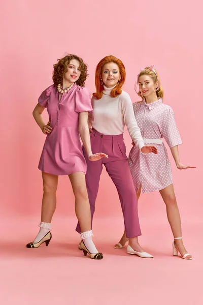 三个漂亮的年轻女子穿着优雅 时尚的衣服 发型和在粉红工作室背景下化妆的肖像 复古风格 六十岁 青春的概念 小鸡鸡风格 — 图库照片