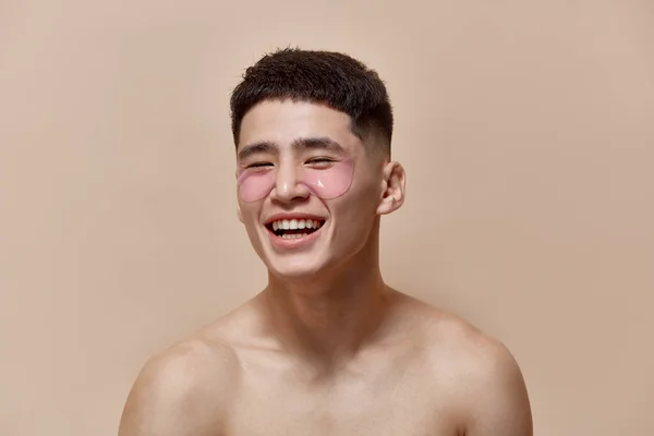 ライトブラウンのスタジオの背景に目のパッチの下で肌の世話をするハンサムな 若い男の肖像画 男性の美しさ スキンケア メンズヘルスの概念 — ストック写真