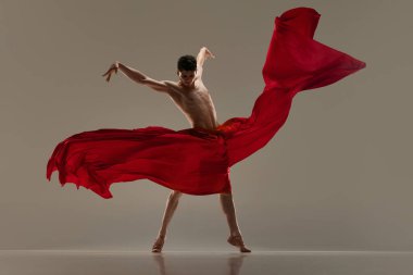 Etkileyici. Yakışıklı genç adam, profesyonel balerin, gri stüdyo arka planında kırmızı ipek kumaşla dans ediyor. Sanat kavramı, klasik dans, ilham, yaratıcılık, güzellik, koreografi