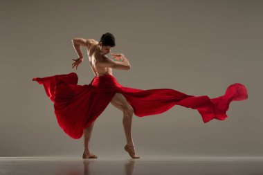 Toreador stili. Gri stüdyo arka planında kırmızı kumaşla dans eden genç bir adamla sanatsal bale gösterisi. Sanat kavramı, klasik dans, ilham, yaratıcılık, moda, güzellik, koreografi