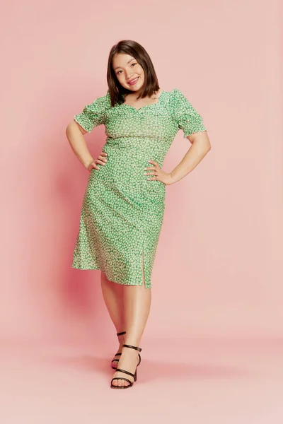 stock image Full-length portrait of young, beautiful, asian girl in stylish green dress, standing, smiling against pink studio background. Concept of emotions, lifestyle, youth, fashion, positivity