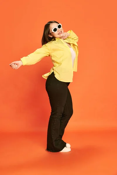 全长的美丽少女画像 戴着时髦的太阳镜和黄色的衬衫摆姿势 在橙色工作室的背景下跳舞 生活方式 庆祝的概念 — 图库照片