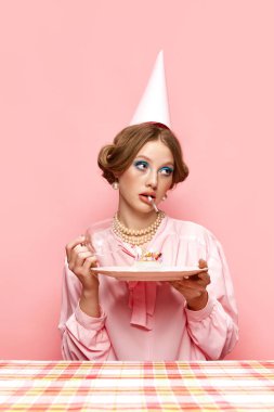 Parlak makyajlı, sigaralı, pembe stüdyo arka planında doğum günü pastası tutan güzel bir genç kız. Kutlama. Yemek ve sanat fotoğrafçılığı. Retro stil kavramı, yaratıcı vizyon, hayal gücü.