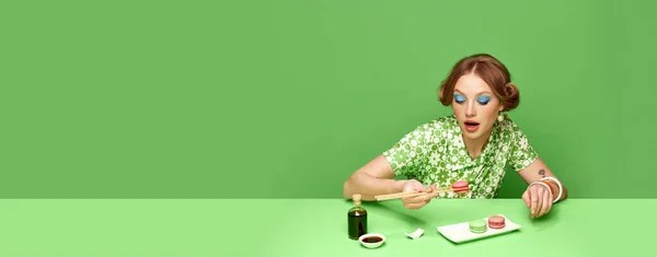 緑のスタジオを背景に醤油でマカロンを食べるスタイリッシュな若い女の子 変な味だ フードポップアート写真 レトロなスタイル 創造的なビジョン 想像力の概念 バナーだ 広告のコピースペース — ストック写真
