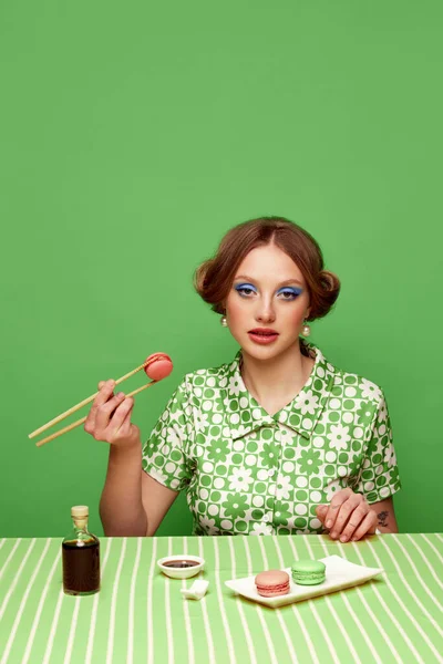 緑のスタジオの背景に箸でマカロンを持つ美しい少女の肖像画 醤油味 フードポップアート写真 レトロなスタイル 創造的なビジョン 想像力の概念 — ストック写真