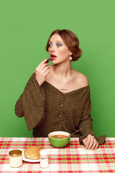 緑のスタジオの背景に野菜スープを食べる明るいメイクを持つかなり若い女の子 夕食の時間だ フードポップアート写真 レトロなスタイル 創造的なビジョン 想像力の概念 — ストック写真