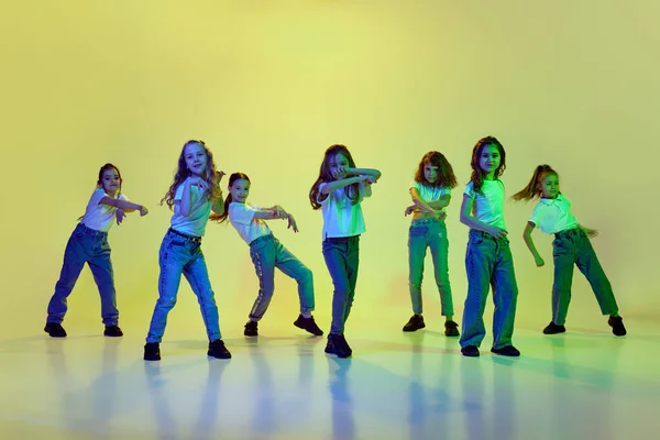 小さな女の子のダイナミックなイメージ ネオンで緑のスタジオの背景に合わせて踊る子供たち 普段着 ヒップホップスタイル 子供時代 スポーツライフスタイル 行動と運動の概念 — ストック写真