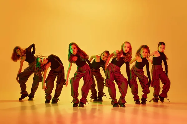Etkileyici bir dans. Bir grup şık küçük kız, çocuklar, dans, hip-hop eğitimi neon ışıkta sarı stüdyo karşısında. Çocukluk kavramı, hobi, spor yaşam tarzı, eğitim