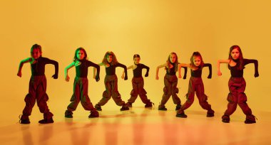 Bir grup sanatçı, küçük dansçılar, kızlar, şık giyinmiş çocuklar, neon ışıkta sarı stüdyo arka planına karşı hip-hop dansı yapıyorlar. Çocukluk kavramı, hobi, spor yaşam tarzı