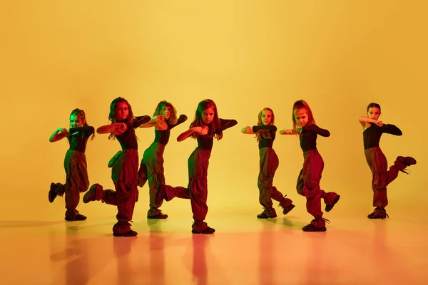 时髦的 一群孩子 穿着运动型休闲装的小女孩跳嘻哈舞 在霓虹灯下凝视着黄色的工作室背景跳舞 业余爱好 体育生活方式的概念 — 图库照片