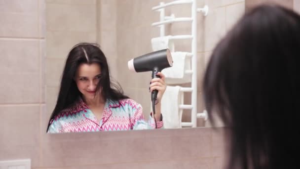 肯定的な カラフルなホームウェアの若い女性は パジャマは ファンと髪を乾燥させ バスルームで朝に準備を取得します 日付のために遅い 肯定的な気分 — ストック動画