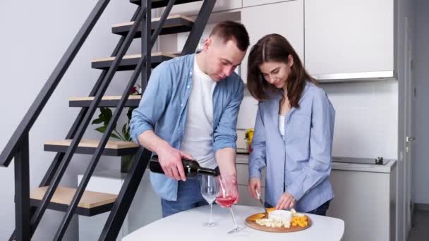 ロマンチックなディナーの準備 自宅で休日を祝う美しい若いカップル 妻のカッティングチーズ 夫は赤ワインを注ぐ ライフスタイル サポートの概念 — ストック動画