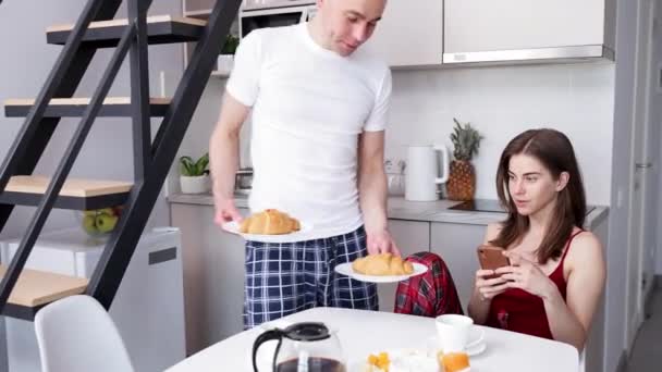 キッチンで朝食を共にする幸せな笑顔のカップル 美しい彼女にクロワッサンを出す男 ライフスタイル サポートとケアの概念 — ストック動画