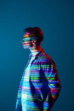Fütürist vizyon. Çok renkli dijital çizgileri olan günlük kıyafetlerle yakışıklı genç adam mavi arka planda duran vücudu yansıtıyor. Modern fotoğrafçılık, sanat, siber punk, yaratıcılık kavramı
