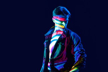 İnsanoğlunun yaratıcılığı. Dijital neon filtre yansıması olan yakışıklı genç adam koyu arkaplanda poz veriyor. Modern fotoğrafçılık, sanat, siber punk, tekno, yaratıcılık, gelecekçilik kavramı