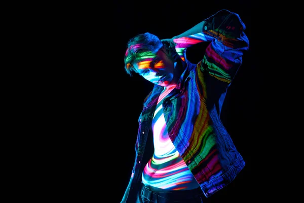 Handsome young male model posing with digital neon filter with multicolored lights reflection on body over dark background. Concept of modern photography, art, cyberpunk, techno, creativity, fashion