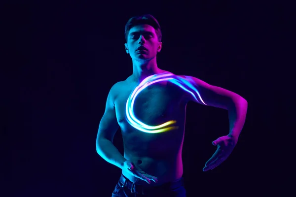 Fantasy. Handsome young man posing shirtless with digital neon filter reflection on body over dark purple background in neon light. Concept of modern photography, art, cyberpunk, techno, creativity