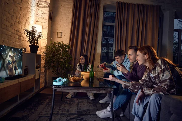 若い陽気な人々のグループは 友人のソファの上に自宅で夜に座って 一緒にコンソールボクシングの競争でプレーし 楽しみを持っている 友情の概念は レジャー活動 オンラインゲーム — ストック写真