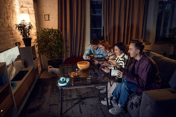 若い男性と女性のグループは 自宅で一緒に時間を過ごし 夕方にソファに座って コンソール上でオンラインゲームをプレイします モトスポーツ レジャー活動 楽しみの概念 — ストック写真