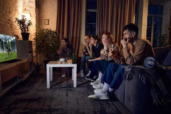 若者のグループ 夕方に自宅でソファに座っている友人やテレビでライブサッカーの試合翻訳を見て レジャー活動 楽しみ 感情の概念 — ストック写真