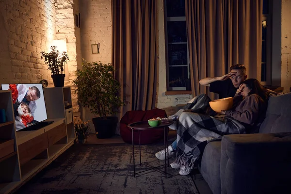 若い美しく 感情的なカップル 男性と女性は夕方に自宅で時間を過ごし ソファに座って医師とテレビ番組を見ています 関係の概念 レジャー活動 — ストック写真