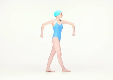Mavi mayo ve yüzme şapkalı genç kız beyaz arka planda geniş elleri olan bir pozisyonda duruyor. Eski tarz, spor, moda, gençlik, klasik. İlan için alanı kopyala