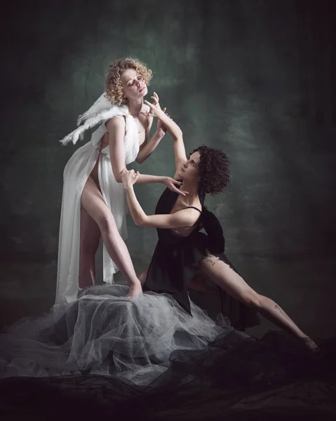 Portrait of two women, angel and demon against dark, green, vintage background. Temptation and tenderness. Life balance. Concept of history, remake, good and bad, creative photography