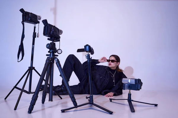 身穿时髦黑色衣服 戴着时髦太阳镜的年轻貌美的女孩用复古相机拍摄视频 摆出一副工作室的样子 90年代风格 复古和复古 小玩意 — 图库照片