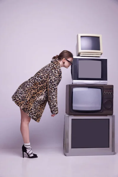 動物のプリントコートのスタイリッシュな若い女の子とグレーのスタジオの背景にレトロなテレビセットにもたれて流行のサングラス ニュースだ ファッション 80年代 90年代スタイル レトロとヴィンテージ マスメディアの概念 — ストック写真